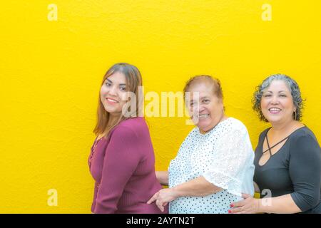 Granddaughter, grandmother and daughter taken from the waist very happy, three generations of smiling Mexican women wearing casual clothes in a row lo Stock Photo