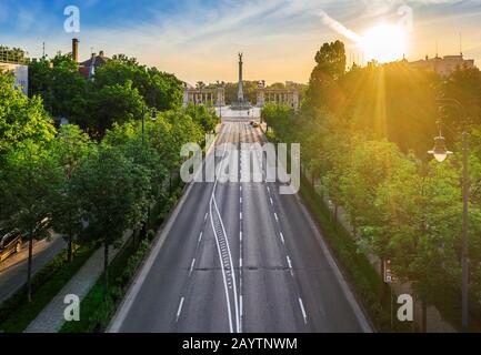 Budapest, Hungary - Aerial drone view of totally empty Andrassy street at sunrise with green trees and sunlight and Heroes' Square (Hosok tere) at bac Stock Photo