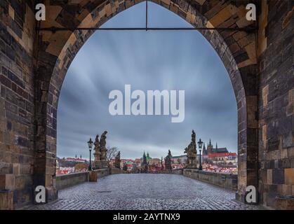 Prague, Czech Republic - Entrance of the world famous Charles Bridge at the Old Town Bridge Tower on a winter morning with moving clouds. St.Vitus Cat Stock Photo