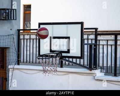 Red-white basketball flying in a net attached to metal black fence Stock Photo