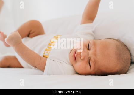 Sad small Asian infant in pajama with closed eyes crying newborn baby lying on bed at home Stock Photo
