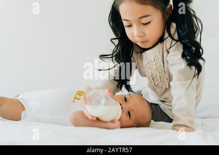 Boy feeding milk to brother from baby bottle while sitting on sofa at home  Stock Photo - Alamy