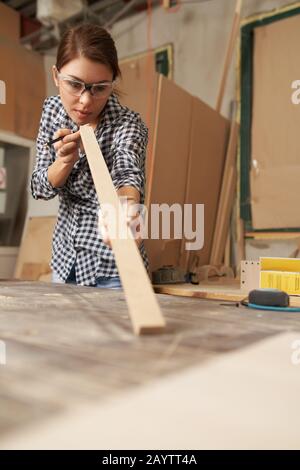Woman carpenter in glasses with wooden dos and pencil in her hands in workshop Stock Photo
