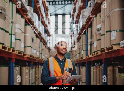 Handsome warehouse worker uses digital tablet for checking stock, on the shelves standing cardboard boxes Stock Photo