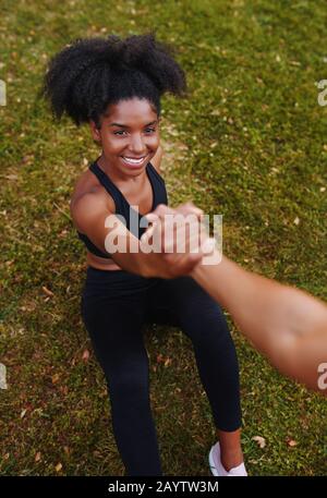 An above view of smiling african american sporty young woman getting help from her friends while doing workouts in park Stock Photo