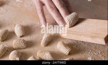 Close up process of homemade vegan gnocchi pasta with wholemeal flour making. The home cook crawls on the special wooden tool the gnocco , traditional Stock Photo