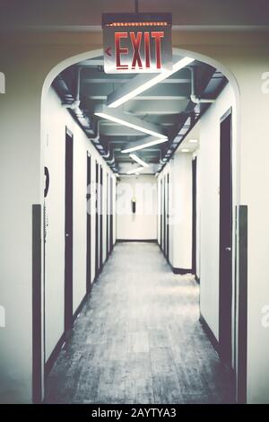 Emergency exit sign in empty corridor, selective focus, color toning applied. Stock Photo