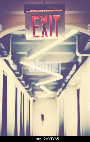 Emergency exit sign in empty corridor, selective focus, color toning applied. Stock Photo