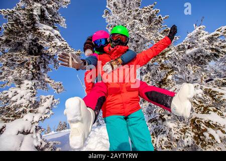 Snowboarder man and woman skier hugging and having fun on background of winter forest and snow. Sunlight in mountains Stock Photo