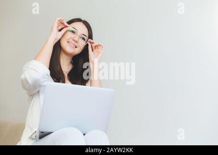 Positve female being glad to finish her course paper, works on laptop computer. Creative female web designer watches video with new graphic ideas, sit Stock Photo