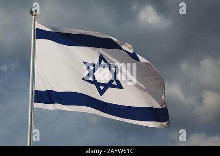 Waving colourful flag of Israel against cloudy sky. Highly detailed fabric texture. Blue and white star against clouds. Jerusalem capital of Israel. I Stock Photo