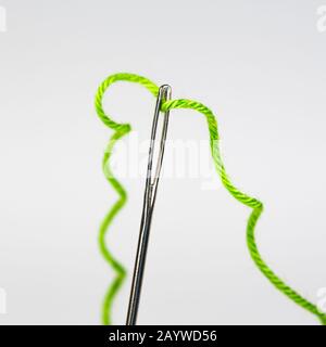 Green thread threaded into the eye of a needle. Close-up with shallow depth of field. Stock Photo