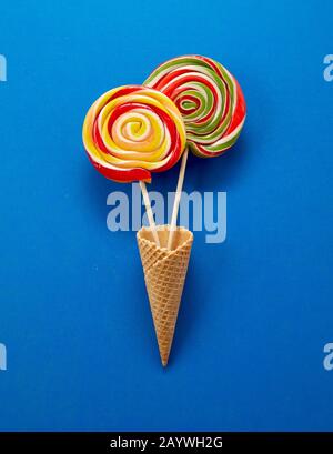 Two colorful spiral lollipops in ice cream cornets over a blue background with copy space Stock Photo