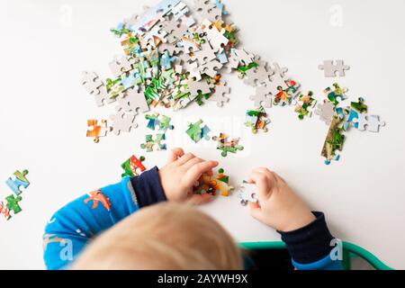 Baby boy solving jigsaw puzzle on the desk, focusing on the hands Stock Photo