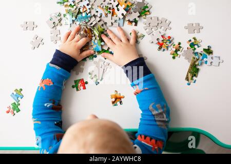 Baby boy solving jigsaw puzzle on the desk, focusing on the hands Stock Photo