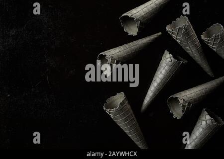 Monochromatic grey background texture of ice cream cones scattered on a black surface with copy space in a flat lay still life Stock Photo