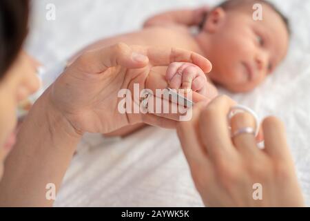 Baby getting fingernails cut while sleeping by his mother with scissors. Nursing a child. Stock Photo
