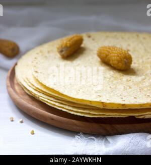 A stack of round corn tortillas on a wooden board and corncobs. Stock Photo