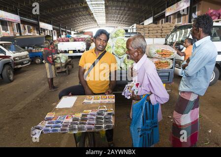 Dambulla, Sri Lanka: 18/03/2019: Inside fruit and vegetable whoelsale market. Men selling lottery tickets.