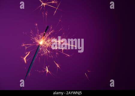 Shiny bright burning bengal fire party sparkler on purple background with copy-space Stock Photo