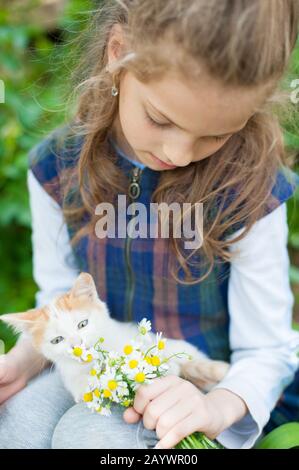 love friendship concept of little girl holding bouquet of daisies with kitty cat smelling smell Stock Photo