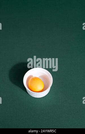 Orange color egg on green background with strong shadow. Minimal modern Easter breakfast background composition. Vertical orientation, top view Stock Photo