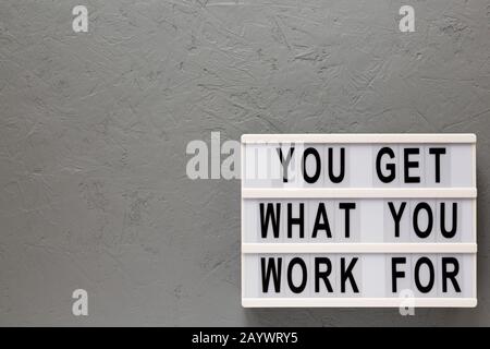 'You get what you work for' words on a lightbox on a gray background, top view. Overhead, from above, flat lay. Space for text. Stock Photo