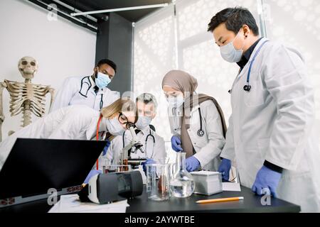 Team of lab workers, veterinarians, bio chemists examining tissues or blood sample using the microscope. Group of multiethnic scietists working with Stock Photo