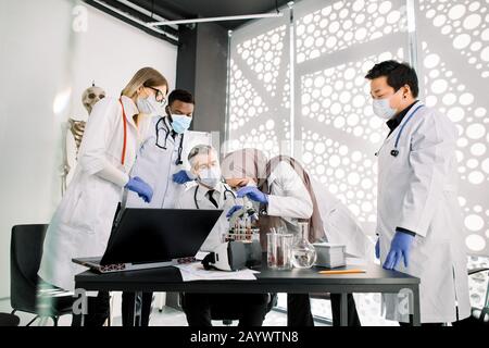 Team of scientists doctors biochemists working with microscope, doing research scientific experiments in laboratory. Muslim woman is looking through Stock Photo