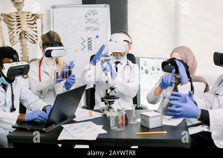 Scientists doctors in coats. gloves and wearing virtual reality glasses working in lab, making medical research. Biotechnology, chemistry, science Stock Photo