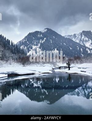 Landscape Photographer with camera on tripod at epic landscape ow winter lake in the mountains with reflection. Stock Photo