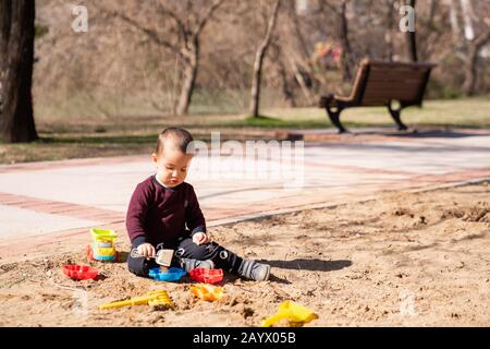 Little cute boy playing in sandbox with plastic toys. Concept play in outdoors in spring or summer time Stock Photo