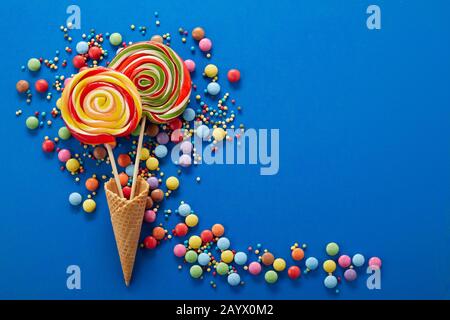 Artistic party background with colorful confectionery with sugar-coated chocolate sweets and sprinkles forming a trail around two spiral lollipops in Stock Photo