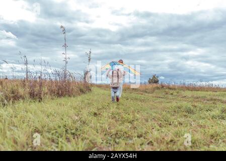 little boy of 4-5 years old, in the autumn launches a kite in a field, happy runs in warm clothes and a beige sweater with a hood. Free space for copy Stock Photo