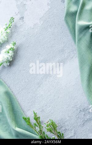 Gray concrete wall surface with frame from thuja branches and green cloth, textured background, copy space, vertical, place for text, top view Stock Photo