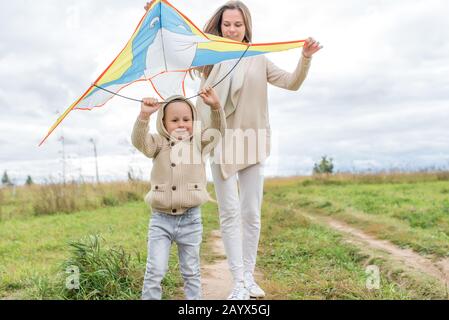 Young family, woman mother happy smiling, little boy in sweater with hood launches kite, rest in field, concept parenting child care and love, parent Stock Photo