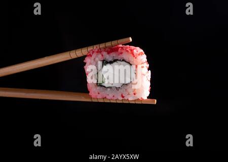 Chopsticks holding seaweed pink roll filled with avocado and fish over black background Stock Photo