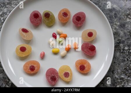 Easter candies in a circle on a white plate on a gray granite table. Concept, High angle view, space for text. Stock Photo