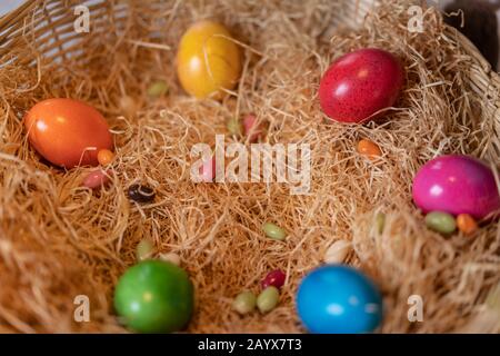 Yellow, red, green, blue, pink and orange colored cooked easter eggs put in a nest of straw in straw basket on white ground. Close up, high angle view. Stock Photo