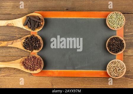 Three wooden cooking spoons and three small wooden bowls filled with different kinds of pepper and an old black slate board with copy space on a rusti Stock Photo