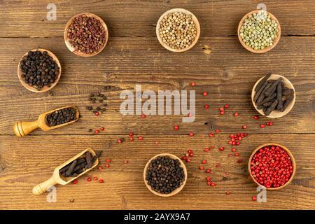 Seven small wooden bowls filled with different kinds of pepper and two wooden spice shovels and red peppercorns lie on a rustic wooden background with Stock Photo