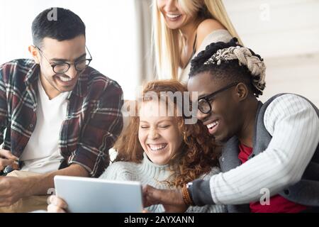Group of cheerful young multi-ethnic friends using tablet while laughing at online video Stock Photo