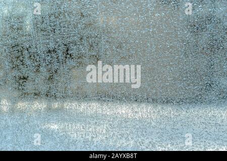 Blurry landscape behind the window and frosted window glass with an impressive natural pattern on a sunny winter day. Close up, abstract background te Stock Photo