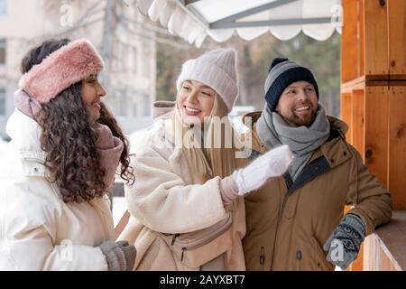 Horizontal portrait of young man and two women discussing something while walking around on winter day outdoors Stock Photo