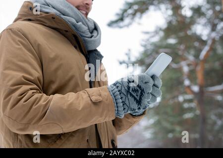 Young man wearing casual warm clothes standing outdoors on winter day using his smartphone, horizontal crop shot Stock Photo