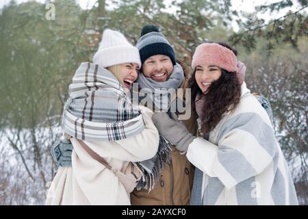 Happy young man and two women smiling and laughing while hugging each other, horizontal winter portrait Stock Photo