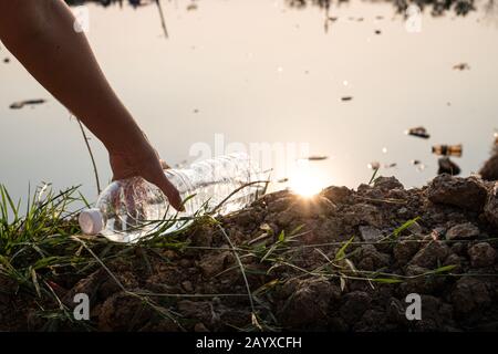 Close up Hand picking up a clear plastic bottle drop on the ground with polluted water background Stock Photo