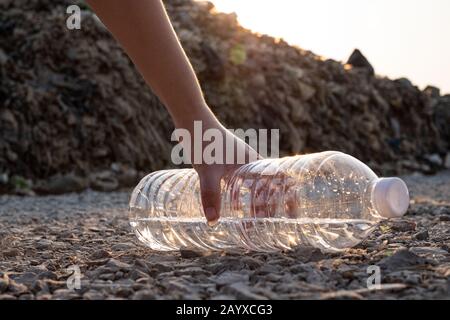 Close up Hand picking up  clear plastic bottle drop on the ground at mountain large garbage background, These waste come from urban and industrial are Stock Photo