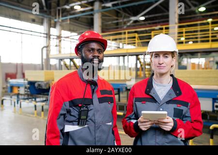 Horizontal portrait shot of two young adult factory engineers in workwear standing together looking at camera Stock Photo