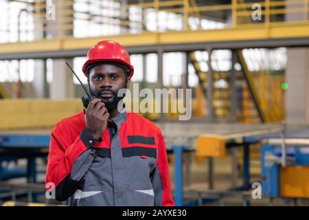 Horizontal portrait shot of professional factory worker using portable radio set to give instructions to his coworkers Stock Photo